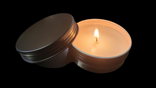 Candle in a metal container with a lit wick on a black background