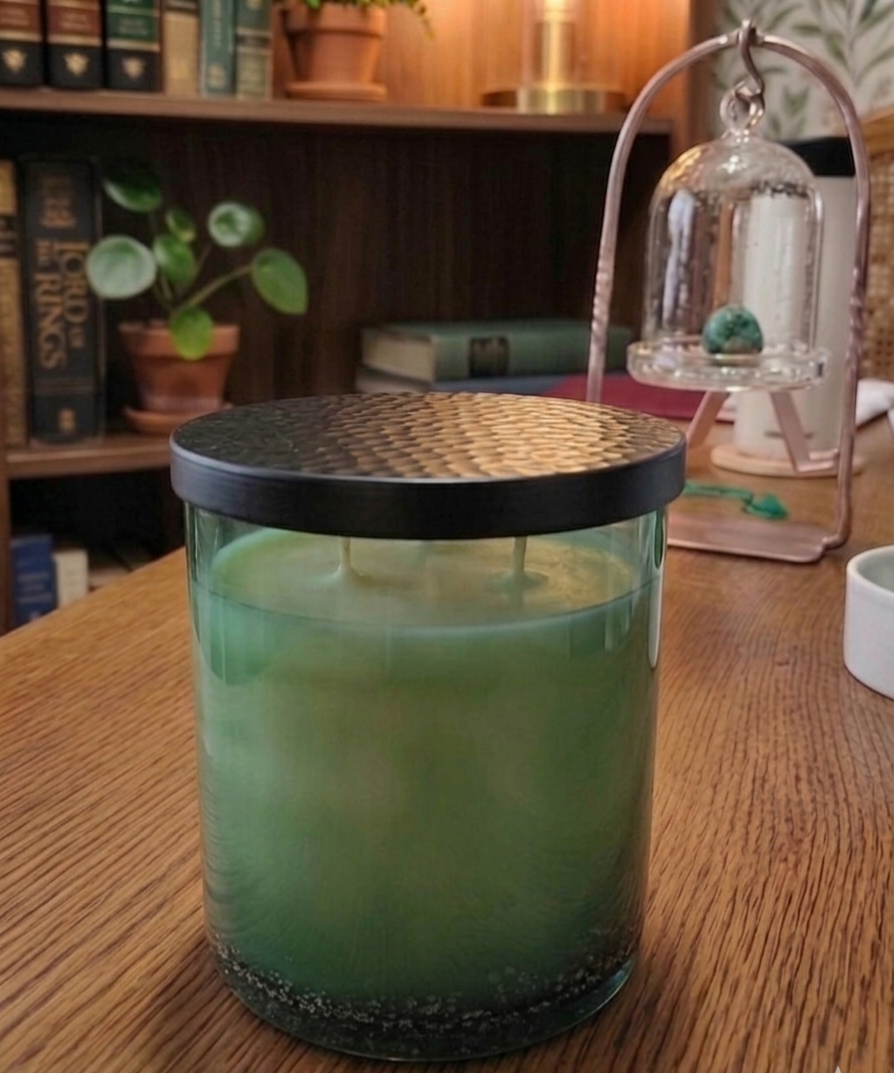 Handblown green glass candle sitting on a wood table with books on a shelf in the background